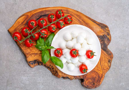 Italian tricolore, small balls of fresh white soft Italian mozzarella cheese, ripe red cherry tomatoes and fresh green basil herb, ready for making caprese salad, close upの写真素材