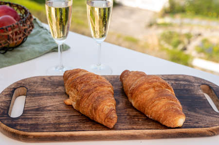 Breakfast with fresh baked croissants and brut champagne sparkling wine in flute glasses served on outdoor cafe or bistro terrace in France or Belgiumの写真素材