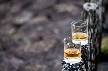 Tasting of dram single malt scotch whiskey on seashore in Scotland, old wooden poles with whiskey glassの写真素材