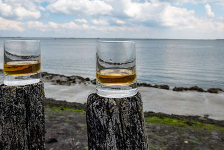 Tasting of dram single malt scotch whiskey on seashore in Scotland, old wooden poles with whiskey...