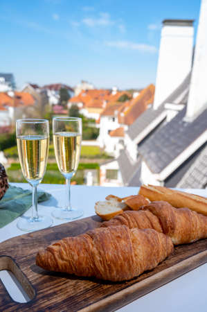 Breakfast with fresh baked croissants and brut champagne sparkling wine in flute glasses served on outdoor cafe or bistro terrace in France or Belgiumの写真素材