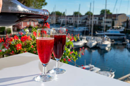 Summer party with kir royal cocktail, pouring of French brut champagne sparkling wine and creme cassis in glasses in yacht harbor of Port Grimaud near Saint-Tropez, French Riviera vacation, Franceの写真素材