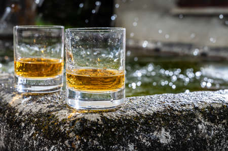 Glasses of strong scotch single malt whiskey served on old stone reservoir for water from mountain spring, Scotlandの写真素材