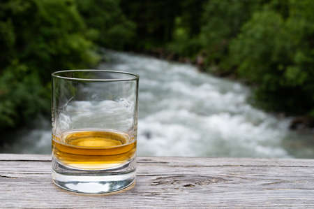 Glass of strong scotch single malt whiskey with fast flowing mountain river on background, Scotlandの写真素材