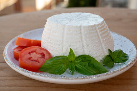 Cheese collection, white Italian soft cheese ricotta served with fresh tomatoes and basil served outdoor with Italian houses on backgroundの写真素材