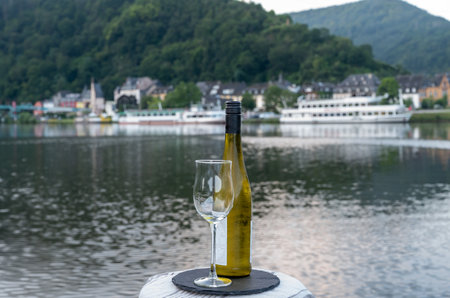 Tasting of white quality riesling wine served on outdoor terrace in Mosel wine region with Mosel river and old German town on background in sunny day, Germanyの写真素材