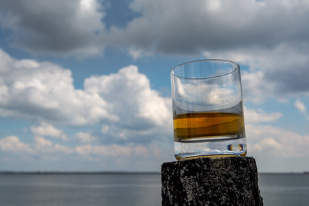 Tasting of dram single malt scotch whiskey on seashore in Scotland, old wooden poles with whiskey glassの写真素材