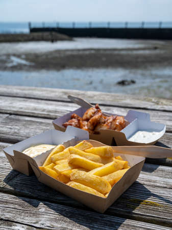 Paper boxes with french fried in oil potato sticks and fish served outdoor