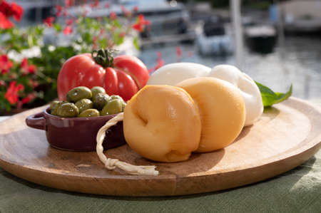 Cheese collection, white and smoked Italian cheese scamorza made from cow milk in South of Italy served outdoor with green olives and red tomatoの写真素材