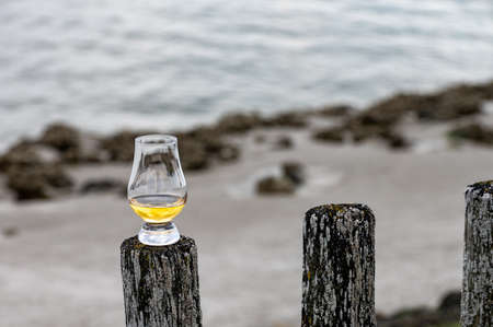 Tasting of dram single malt scotch whiskey on seashore in Scotland, old wooden poles with whiskey glassの写真素材