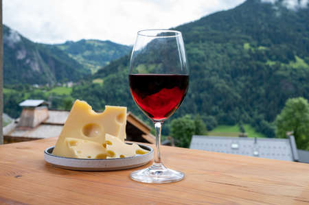 Cheese collection, French cow cheese emmental, glass of red wine from Savoie and french mountains village in Haute-Savoie in summer on backgroundの写真素材