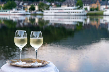 Tasting of white quality riesling wine served on outdoor terrace in Mosel wine region with Mosel river and old German town on background in sunny day, Germanyの写真素材