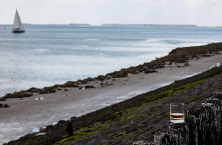 Tasting of dram single malt scotch whiskey on seashore in Scotland, old wooden poles with whiskey glassの写真素材