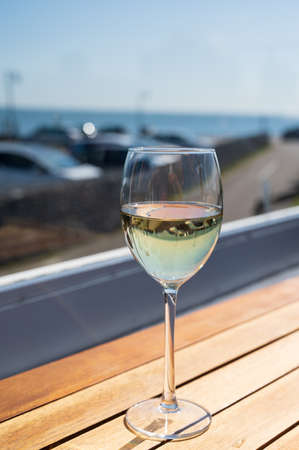 Glass of white wine served on outdoor terrase with seaview in sunny day, summer vacationの写真素材