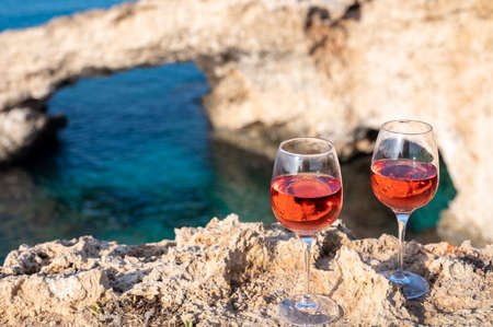 Two glasses of rose dry white wine served on rocks with blue sea bay water and Love Bridge on background near Ayia Napa touristic town on Cyprusの写真素材