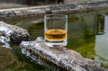 Glass of strong scotch single malt whiskey served on old stone reservoir for water from mountain spring, Scotlandの写真素材