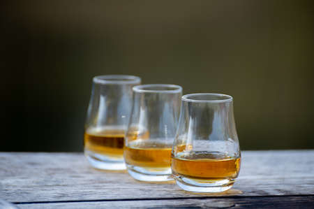 Tasting glasses of finest scotch whiskey strong drink on old outdoor wooden tableの写真素材