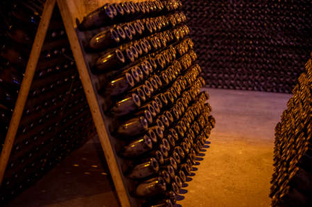Walking in deep and long undergrounds caves with dusty bottles on racks, making champagne sparkling...