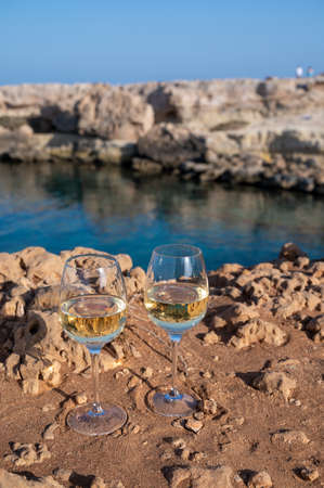 Two glasses of white dry white wine served on yellow rocks in blue sea bay near Protaras touristic...