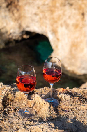 Two glasses of rose dry white wine served on rocks with blue sea bay water and Love Bridge on background near Ayia Napa touristic town on Cyprusの写真素材