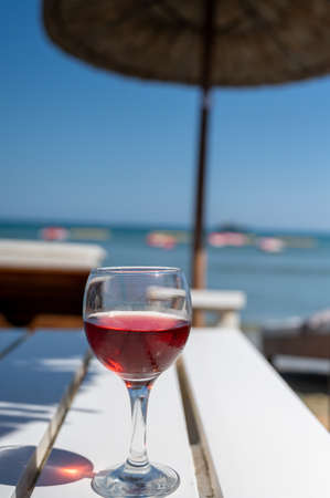 Drinking of cold rose wine in lounge bar on sunny sandy beach with blue sea water on background, summer vacationの写真素材