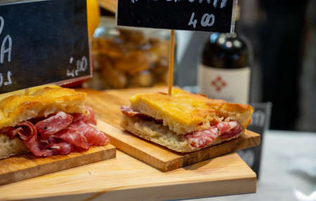 Italian street food, Parma ham sandwiches, bread with cured meats in market in Florence, Italy English translation is: Mortadella from Bologna, Salami from Tuscany and Finocchiona sandwich breadの写真素材