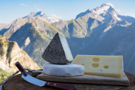 Cheese collection, French emmental, tomme and reblochon de savoie cheeses served outdoor in Savoy region, with Alpine mountains peaks in summer on backgroundの写真素材