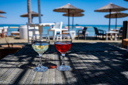 Drinking of cold rose and white wines in lounge bar on sunny sandy beach with blue sea water on background, summer vacationの写真素材
