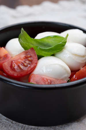 Italian food, tasty caprese salad with red cherry tomatoes, white mozzarella cheese and green basil leavesの写真素材