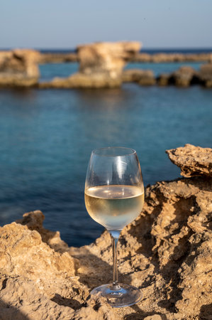 Glass of cold white dry white wine served on rocks with view on blue sea water near Protaras touristic town on Cyprusの写真素材