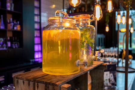 Big glass glass jar with tap filled with fresh healthy lemon lemonade drink served in bar for party...