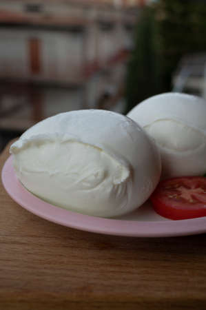 White ball of Italian soft cheese Mozzarella di Bufala Campana served with fresh green basil and red...
