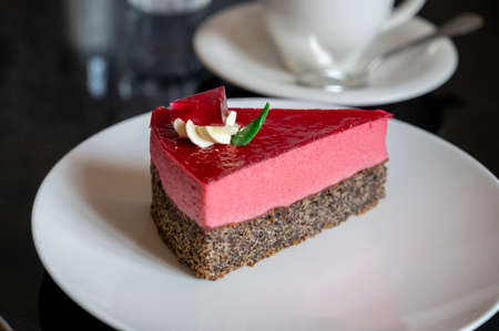 Piece of famous Poppy seed cake with raspberry mousse of Austrian origin served with whipped cream and cup of coffee in old classic cafe-restaurant in Viennaの写真素材