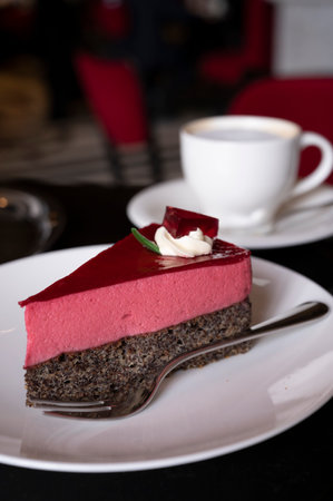 Piece of famous Poppy seed cake with raspberry mousse of Austrian origin served with whipped cream and cup of coffee in old classic cafe-restaurant in Viennaの写真素材