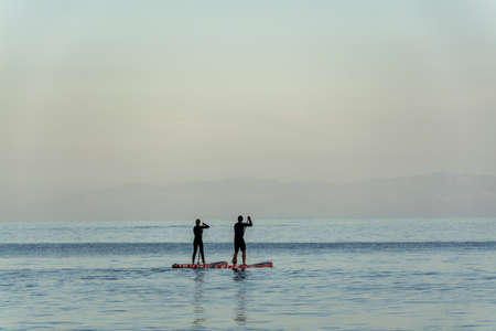 Silhouettes of people on paddle surf boards in Antlantic ocean on Tenerife island at blue sunsetの写真素材