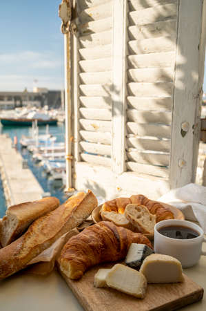 French breakfast with fresh baked croissants, baquett bread, crottin goat cheese, black coffee and view on fisherman's boats in harbor of Cassis, Provence, France. Vacation in Provence.の写真素材