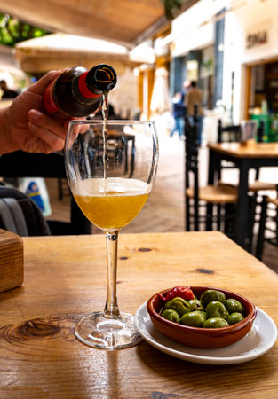 Pouring of beer from bottle in Spanish outdoor cafe and tapas bowl with green olives, Malaga, Andalusiaの写真素材