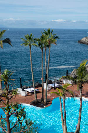 Beach club with blue swimming pool and palm trees on coast of Atlantic ocean, Costa Adeje, Tenerife,...