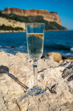 French champagne sparkling wine in glass and view on beach, blue sea water and mountains in Cassis,...