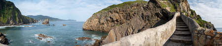 Walking on stone footpath to famous landmark and film location in North of Spain, ocean islet with...