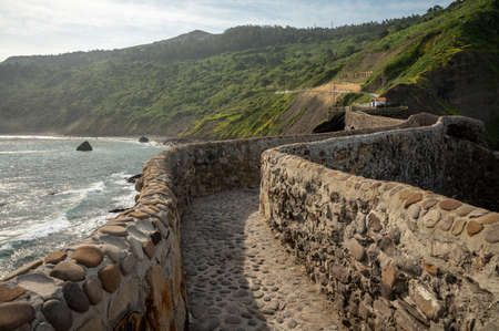 Walking on stone footpath to famous landmark and film location in North of Spain, ocean islet with...