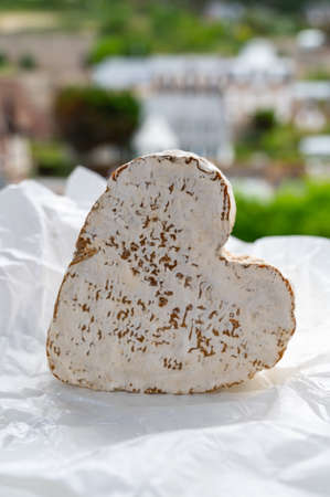 French heartshaped whole piece of neufchatel cow cheese on white paper and view on old houses of...