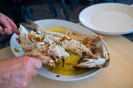 Serving in restaurant of fresh grilled with garlic and olive oil on old charcoal parrillas sea bass...
