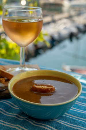 Homemade tasty fish soup with croutons served with glass of cold rose wine and view on colorful fisherman's boats in harbor of Cassis, Privence, France. Food of Provence.の写真素材
