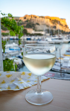 Cold white wine from Cassis winemaking region served in glass on outdoor terrace with view on old fisherman's harbor with colorful boats in Cassis, Provence, Franceの写真素材