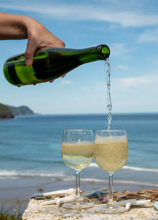 Pouring of txakoli or chacolÃ­ slightly sparkling very dry white wine produced in Spanish Basque Country, served outdoor with view on Bay of Biscay, Atlantic Ocean.の写真素材