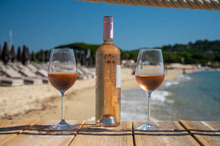 Glasses and bottle of cold rose wine from Provence served outdoor on wooden yacht pier with view on blue water and white sandy beach Plage de Pampelonne near Saint-Tropez, summer vacation in Franceの写真素材