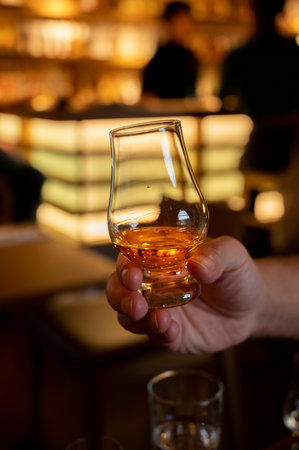Tasting of single malt scotch whiskey in scottish bar in Edinburgh, UK, hand with glass of whisky
