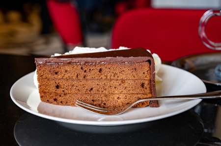 Piece of famous Sachertorte chocolate cake with apricot jam of Austrian origin served with whipped...