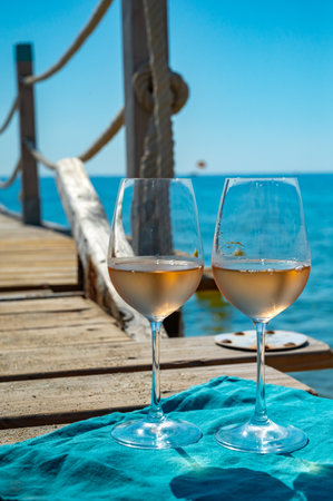 Glasses of cold rose wine from Provence served outdoor on wooden yacht pier with view on blue water and white sandy beach Plage de Pampelonne near Saint-Tropez, summer vacation in Franceの写真素材